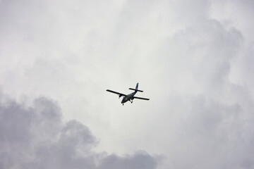 Airplane flying through overcast cloudy sky; minimalist aviation aerial travel scene with white and...