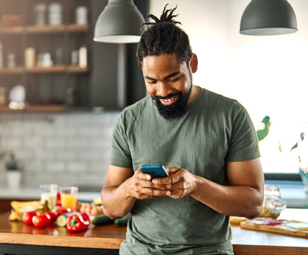 Happy young afro american man having fun preparing food and looking for recipes online using a mobile phone in kitchen, or a young businessman working from home office making connections online, talki - Powered by Adobe