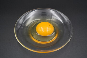 Bright golden yolk resting in a clear dish, showcasing culinary simplicity and the beauty of fresh ingredients in a studio setting