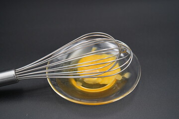 Whisking vibrant egg yolk in a clear bowl on a dark surface during a culinary creation