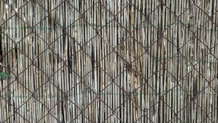 Metal mesh fence with straw rug behind. Natural background.