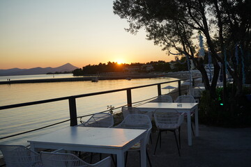 Breathtaking sunset view over a serene shore with white tables set for an evening gathering by the calm waters of a coastal town