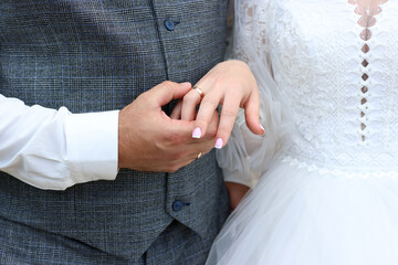 The groom holds the bride's hand with a wedding ring in his hand.