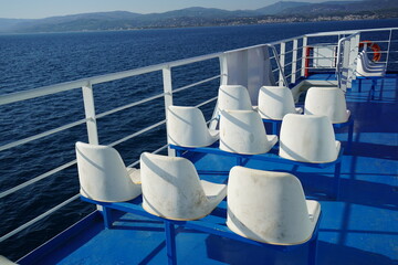 Seats arranged neatly on a ferry deck overlooking the tranquil blue waters of a seaside region during a bright sunny day, inviting travelers to enjoy the serene views