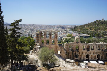 Ancient ruins of Herodes Atticus theater overlook a bustling Athens, sunlit hills and vibrant city life blend in perfect harmony at midday