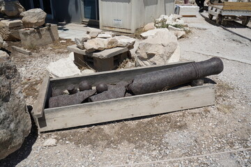 Ancient artillery remnants lie casually in a wooden crate at a historical excavation site near the coast on a bright sunny day