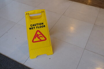 Bright yellow warning sign placed on a tiled floor, alerting pedestrians to a slippery surface to...