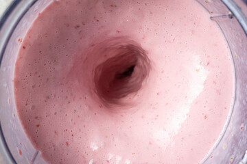 The process of making a strawberry milkshake, whisking all the ingredients in a blender.