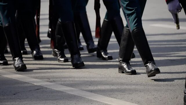 Uniformed soldiers in dark boots march in synchronized formation on an urban street, displaying coordinated movement and discipline during a ceremonial event.