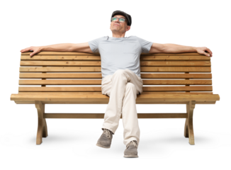 Cheerful mature man in his 50s sitting on a bench with arms resting casually, looking up and smiling. Studio image on white background, dressed in casual clothing with a hat and reading glasses