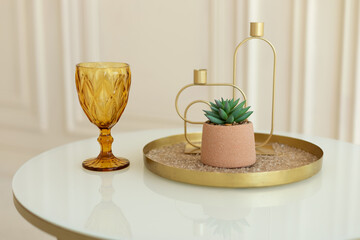 Stylish composition of home with small plant in pot and gold wineglass on coffee table. Modern...