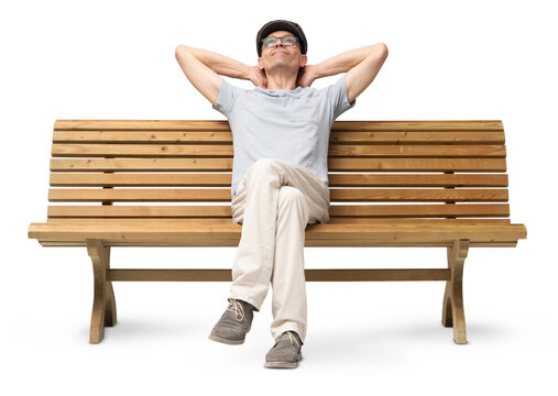 Cheerful mature man in his 50s sitting on a bench with arms resting casually, looking up and smiling. Studio image on white background, dressed in casual clothing with a hat and reading glasses