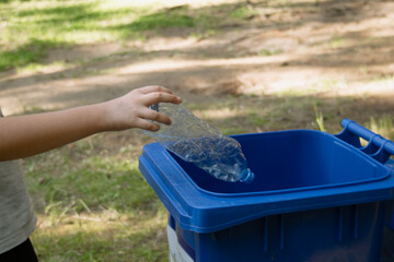 children clean up the forest by throwing empty bottles into a bag and a trash can