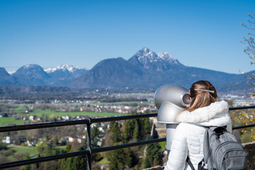 Mujer turista usando uno de los telescopios del castillo de Salzburgo para admirar las vistas de los Alpes Austríacos