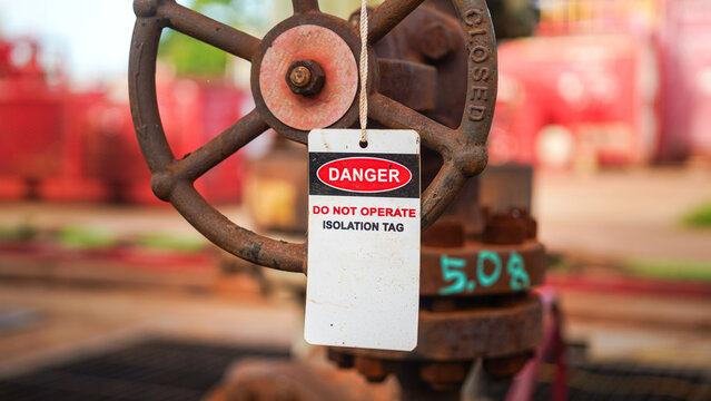 Isolation tag or lockout tagout which is hanged on pipeline valve that under maintenance, do not operate. Industrial safety sign object, close-up.