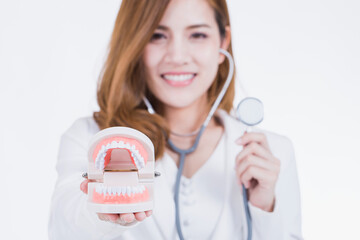 Smiling Southeast Asian female dentist wearing white coat, holding dental model and stethoscope....