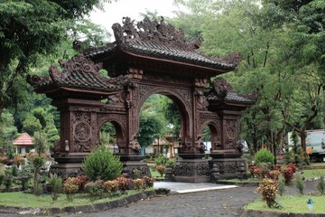 Ornate brown stone gateway with arches framed by trees in a parklike setting with a stone path