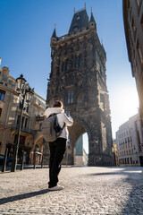 Mujer turista paseando por la ciudad de Praga y tomando fotos, con la torre de la pólvora y el sol naciente de fondo.	