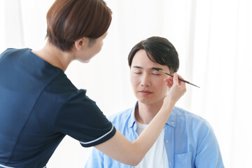 美容部員に眉毛のメイクをしてもらう男性