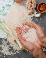 Hand Holding Raw White Rice Grains Over a Bowl,  A hand is holding a handful of white rice. The rice is scattered all over the ground. The hand is positioned in the middle of the rice
