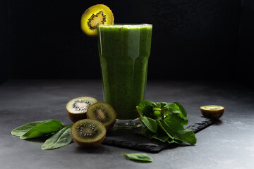Healthy green smoothie in a glass on a black background. Spinach, kiwi, and banana smoothie with...