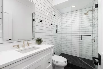 Fototapete A white bathroom with subway tile walls, gold faucets, and black square tile flooring. © Joseph Hendrickson