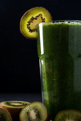 Healthy green smoothie in a glass on a black background. Spinach, kiwi, and banana smoothie with mint