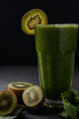 Healthy green smoothie in a glass on a black background. Spinach, kiwi, and banana smoothie with mint