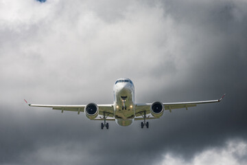 Front view of commercial jet airplane on final approach with landing gear deployed, aviation photo of twin engine aircraft flying under stormy sky with dramatic clouds, captured in daylight
