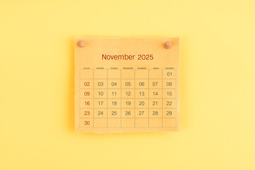 November 2025 brown calendar with wooden thumbtack on yellow color background.