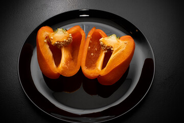 Orange bell pepper, half and slices isolated on black plate. Concept food preparation process.