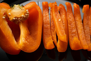 Orange bell pepper, half and slices isolated on black plate. Concept food preparation process.