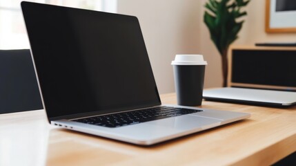 Fototapeta premium Sleek laptop and black coffee cup on a wooden desk in a modern, minimalistic workspace with plants and framed art in the background.