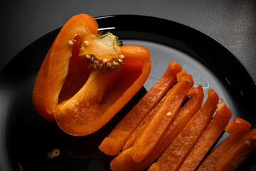 Orange bell pepper, half and slices isolated on black plate. Concept food preparation process.