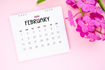 February 2026 desk calendar and pink orchid on pink color background.