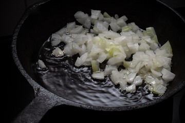 Home cooking. Onions are fried in a cast iron skillet on a hot pan with vegetable oil. Close-up.