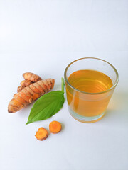 Cold turmeric drink, glass cup of turmeric drink. Fresh cut turmeric root and green leaves on white...