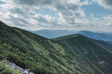 Mountain landscape with hiking trail on the ridge. Cloudy sky with cumulus clouds. Scenic view of mountain peaks, perfect for travel, trekking, and outdoor nature themes.