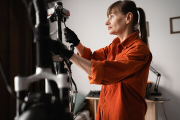 Middle aged woman repairing bicycle at home doing her favorite hobby