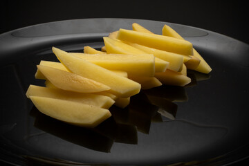 Raw potatoes cut into large strips on a black plate, top view, side view. Cooking delicious French...