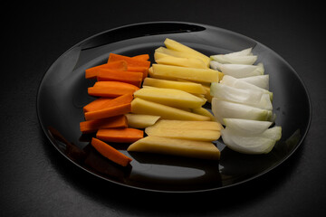 Raw potatoes cut into large strips, raw carrots cut into strips and onions cut into strips on a...