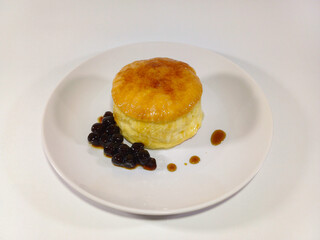 Golden-brown souffle pancake on a plain white plate, accompanied by a small pile of dark berry preserves and a drizzle of syrup, showing a delicate and airy dessert, brunch or breakfast item
