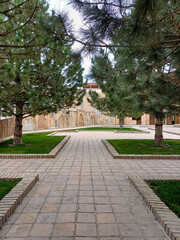 Fototapeta premium Serene park pathway made of light-colored square tiles, framed by symmetrical green trees and grass, depicting a peaceful urban landscape. Related to historical sites, public spaces, tranquility