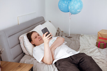 Teen boy checking social media holding smartphone, using mobile phone app playing game, relaxing on...