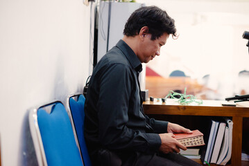 Thoughtful Man Holding Book in Room, Contemplating, Reading, with Blue Chairs Beside
