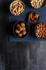 Bowls with nuts and blue table cloth on black chalkboard background. Flat lay. Top view.