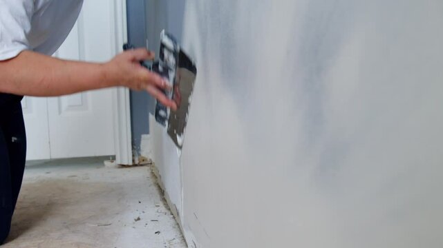 With A Calm, Steady Hand, This Woman In Work Gloves Applies A Thin, Even Layer Of Putty Onto A White Wall For Perfect Surface Restoration.
