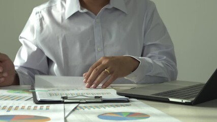 Young asian businessman is reading and checking paper documents, signing the contract to send to business partner, preparing research and data analysis with laptop or computer as a remote freelancer. - Powered by Adobe
