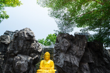 Gold Buddha for respect and also the other statue surrounded by imitated rocks. At Wat Lak Si Rat Samosorn A Buddhist public temple in Samut Sakhon, Thailand 