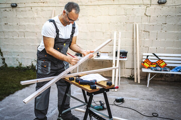 Mature male carpenter measuring wooden plank outdoors